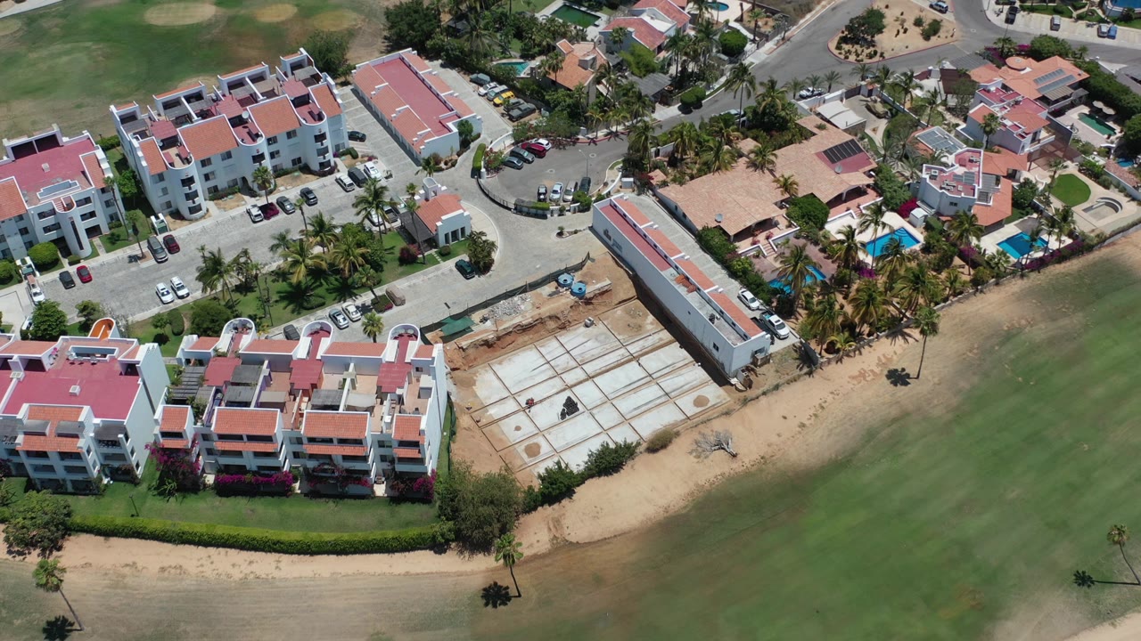 Aerial view of red-roofed residences beside sandy construction plots and green grounds.