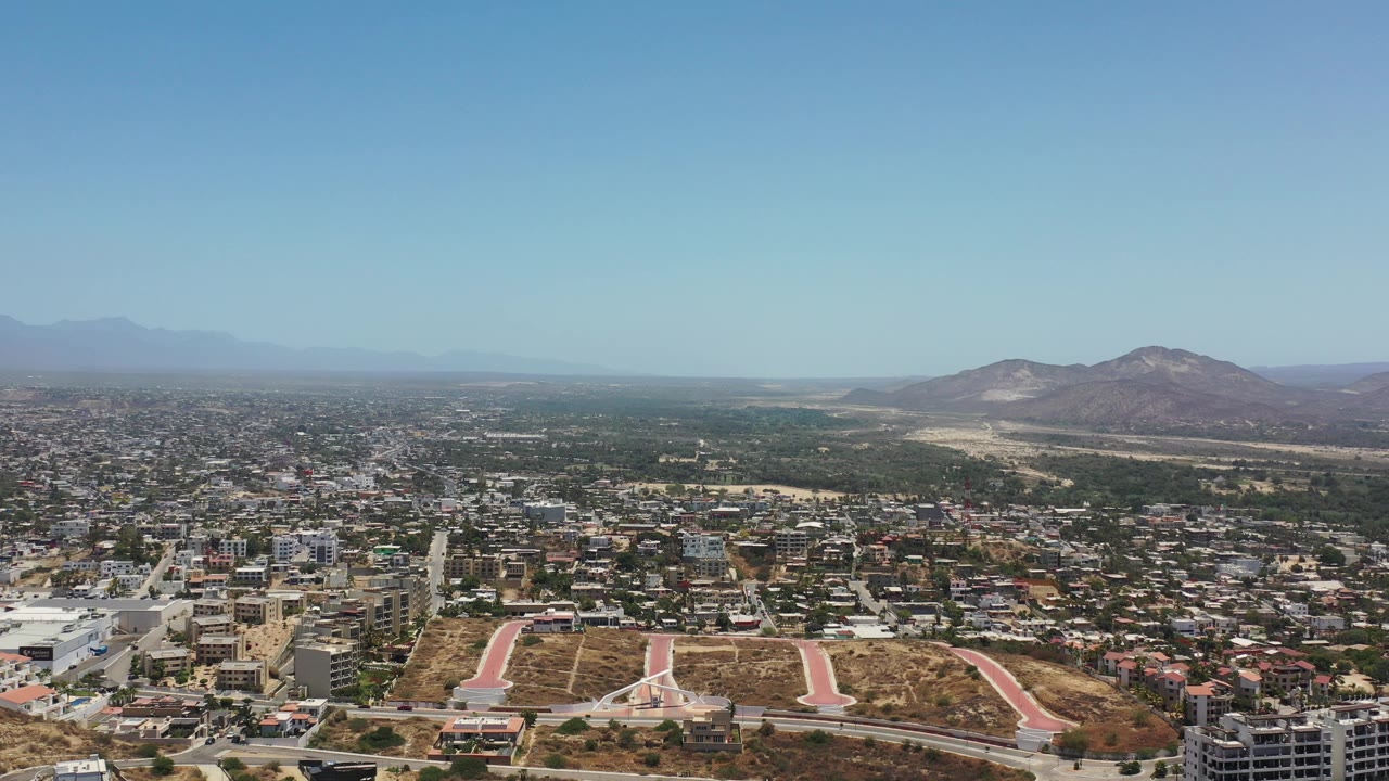 Wide aerial city view with mountains and blue sky.