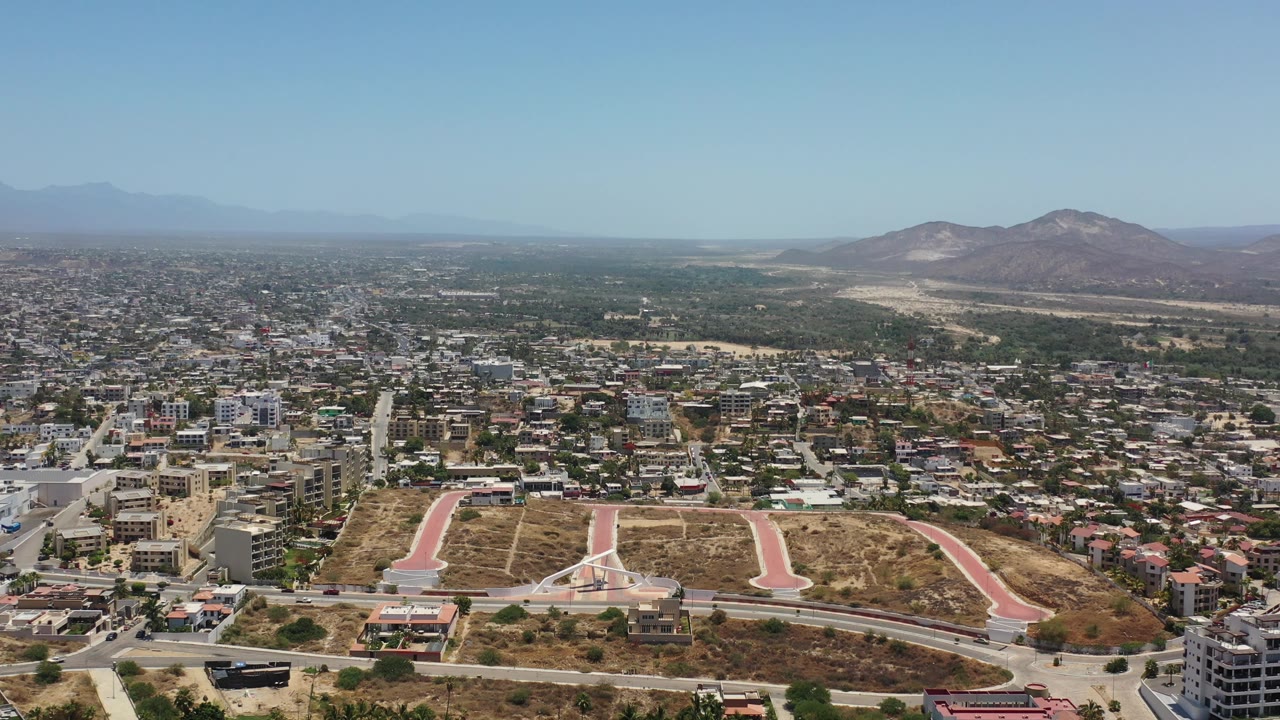 High drone view of Los Cabos cityscape with desert lots and mountains.