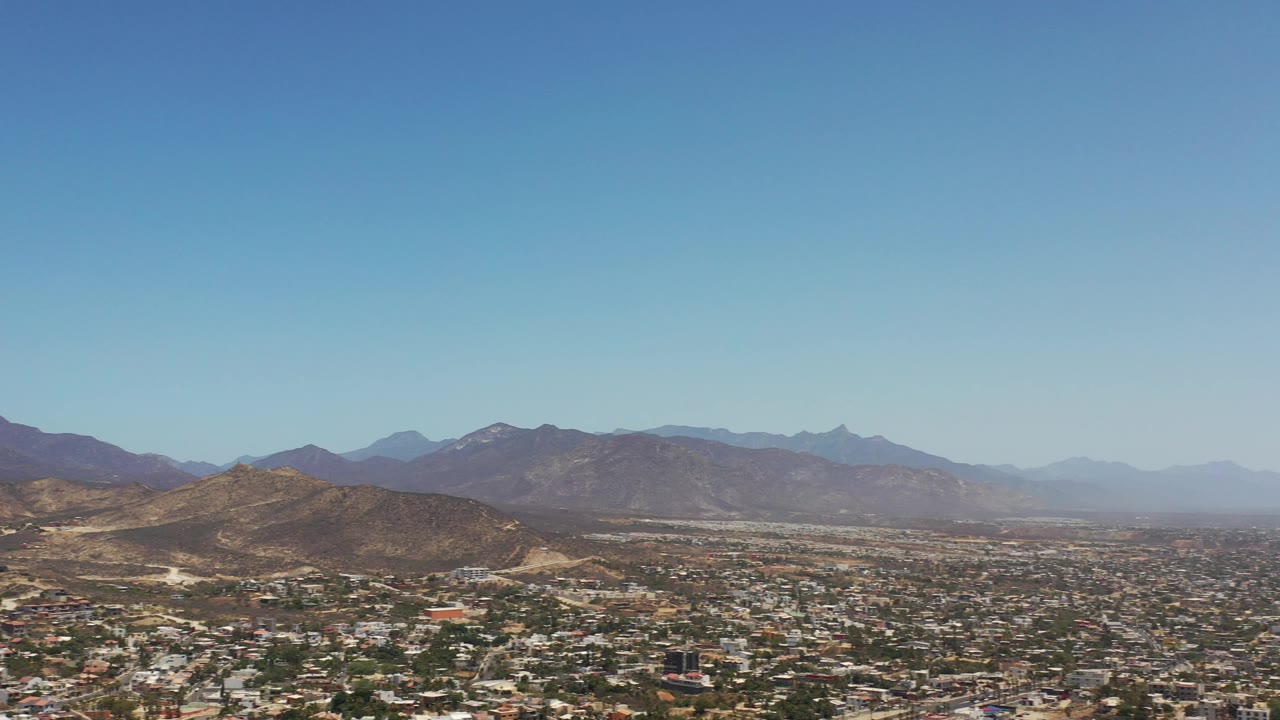 Wide aerial view of town, desert hills, and distant mountains under blue sky
