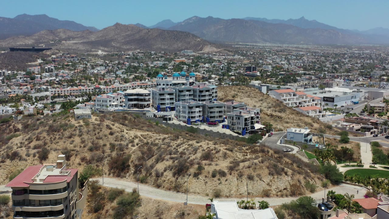 Wide aerial view of dry hillside homes, valley development, and distant mountains.