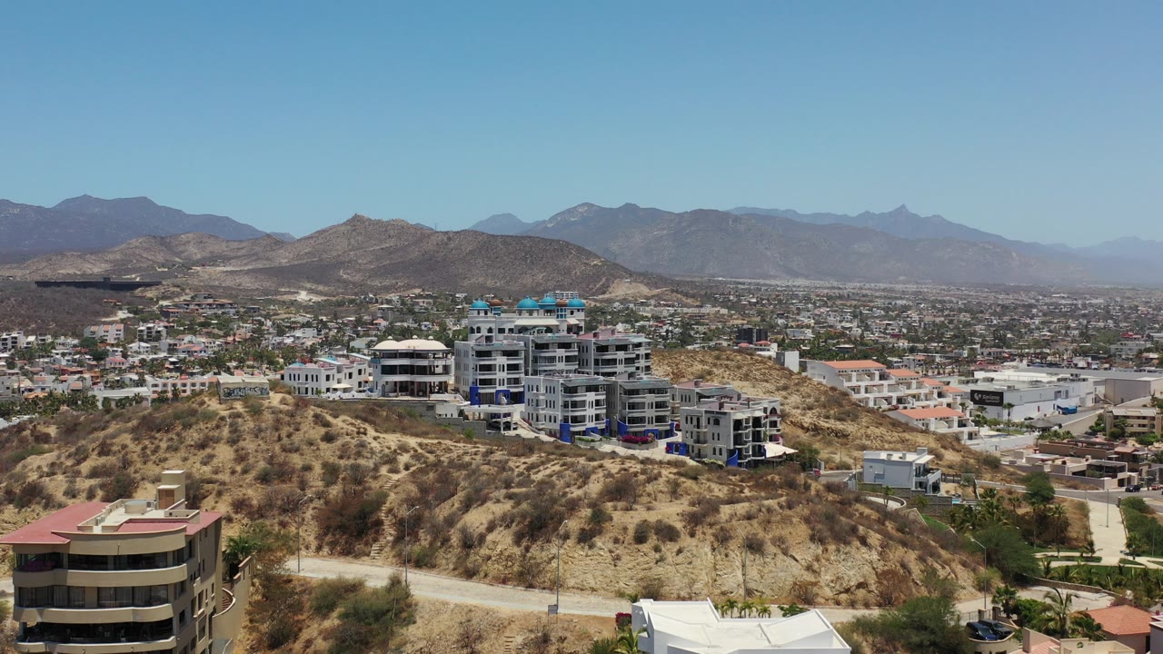 Hillside apartment buildings above a dry city valley and mountains.