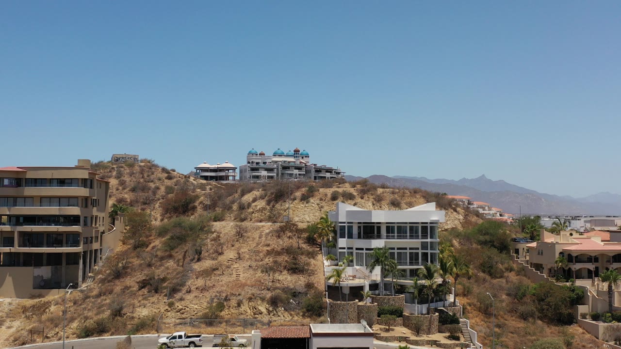 Modern villas on a dry rocky hillside under a clear blue sky.