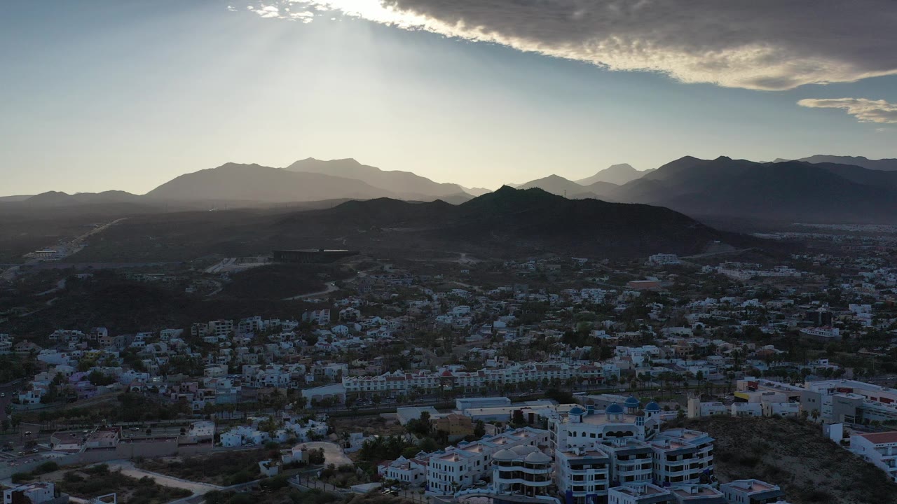 Aerial view of a city below mountains with sunlit cloud cover.