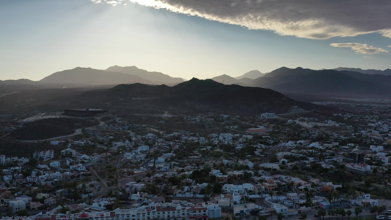 Wide aerial town view with mountains and sunlit cloud overhead
