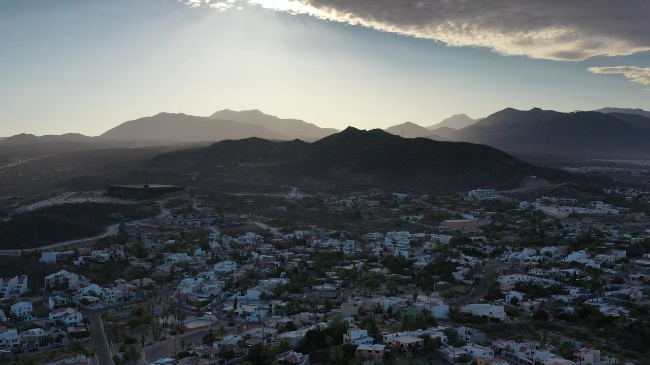 Aerial view of a town below dark mountain ridges at sunrise.
