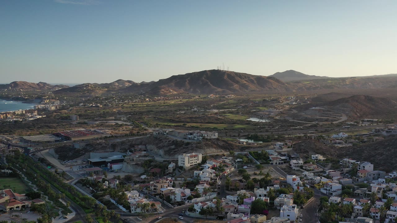 Wide aerial view of homes, hills, water, and mountains.
