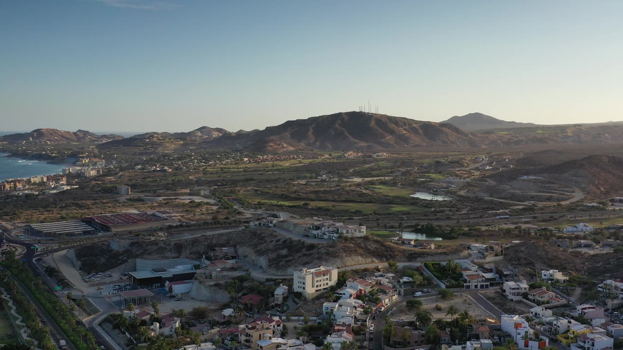 High drone view over houses, open land, blue water, and brown mountains