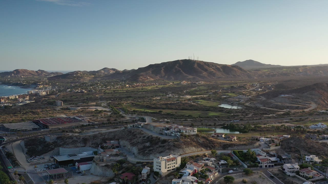 Wide aerial view of mountains, roads, homes, and coastal water.