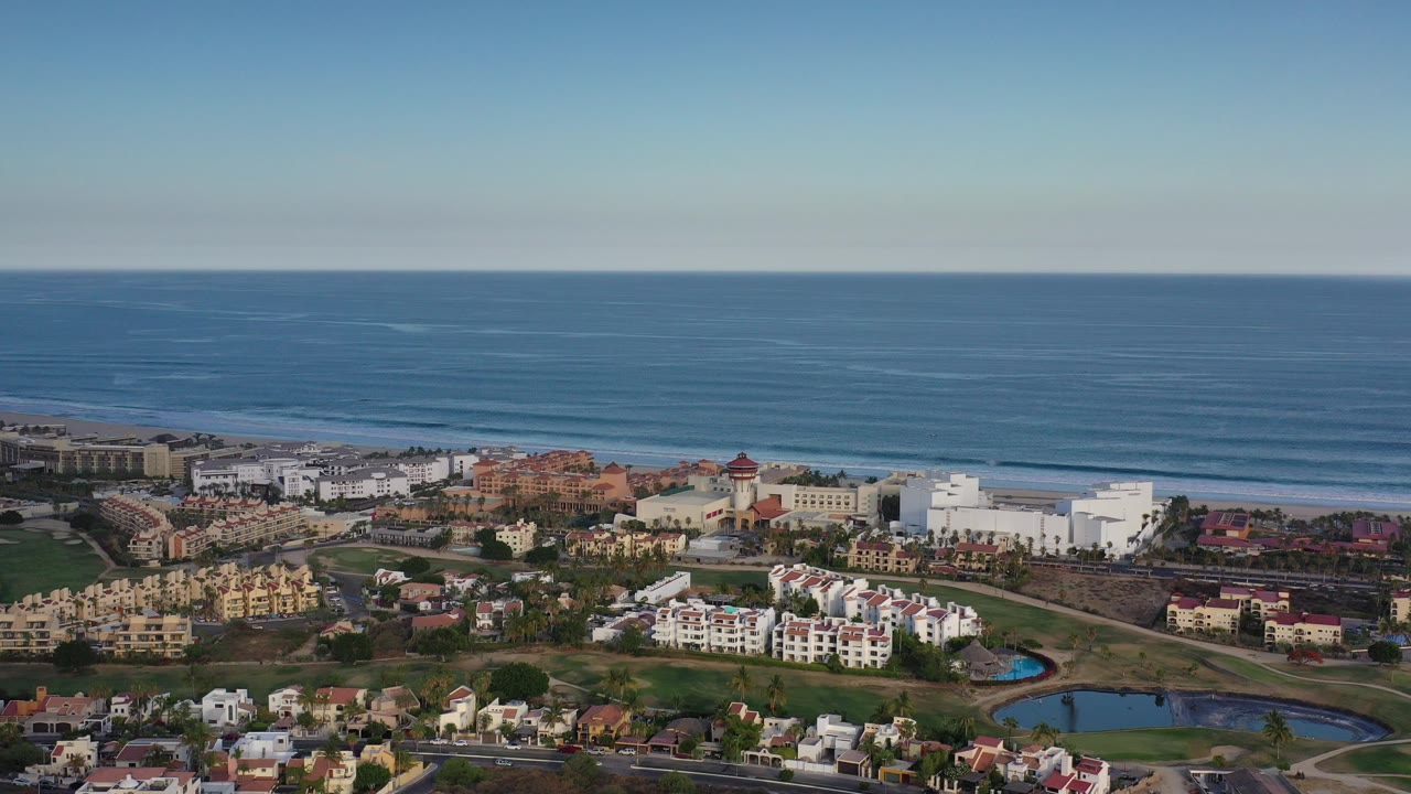 Wide aerial view of coastal buildings, ponds, and ocean horizon.