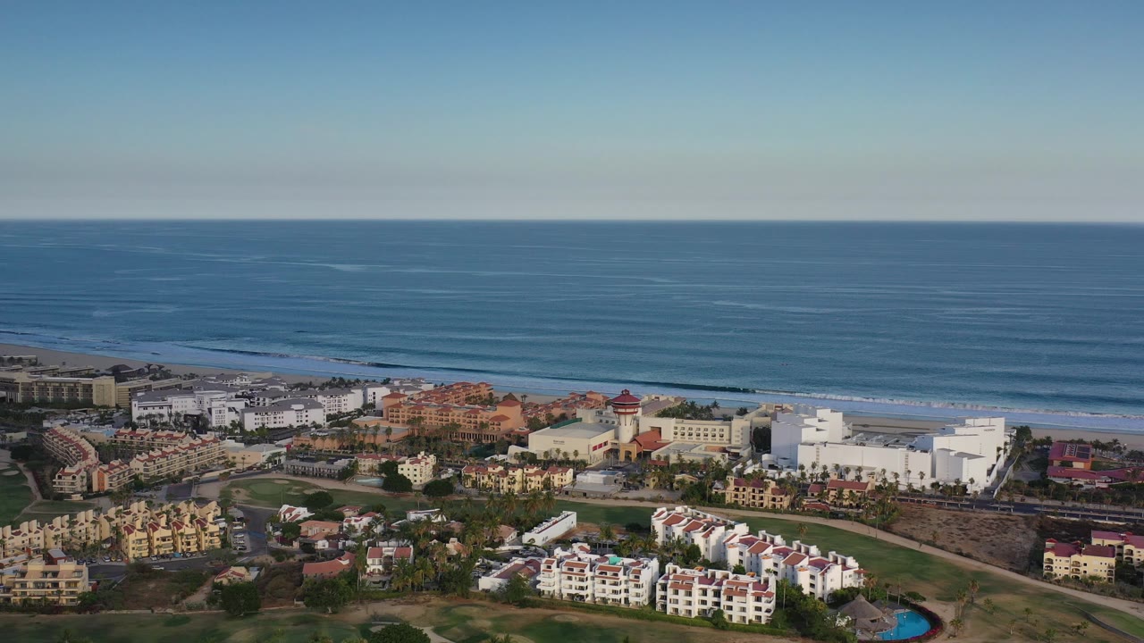 Coastal city buildings, beach, and calm ocean seen from above.
