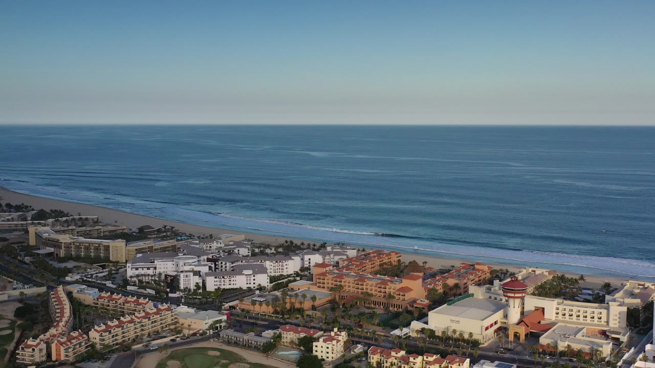 Aerial view of coastal resort buildings beside a beach and blue ocean waves.