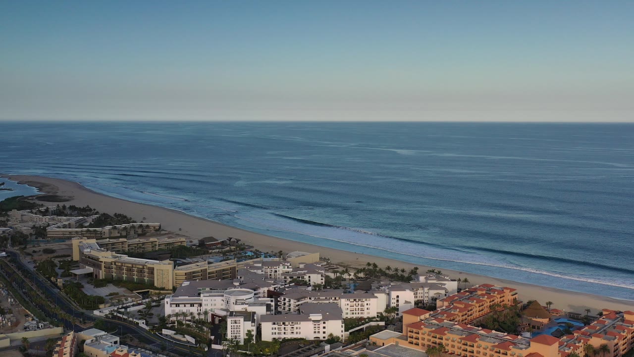 Aerial view of beachfront buildings beside a blue ocean and sandy beach.