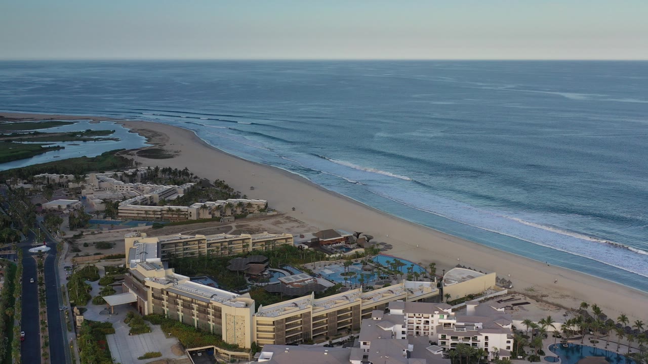 Aerial view of beach, ocean surf, buildings, pools, and road