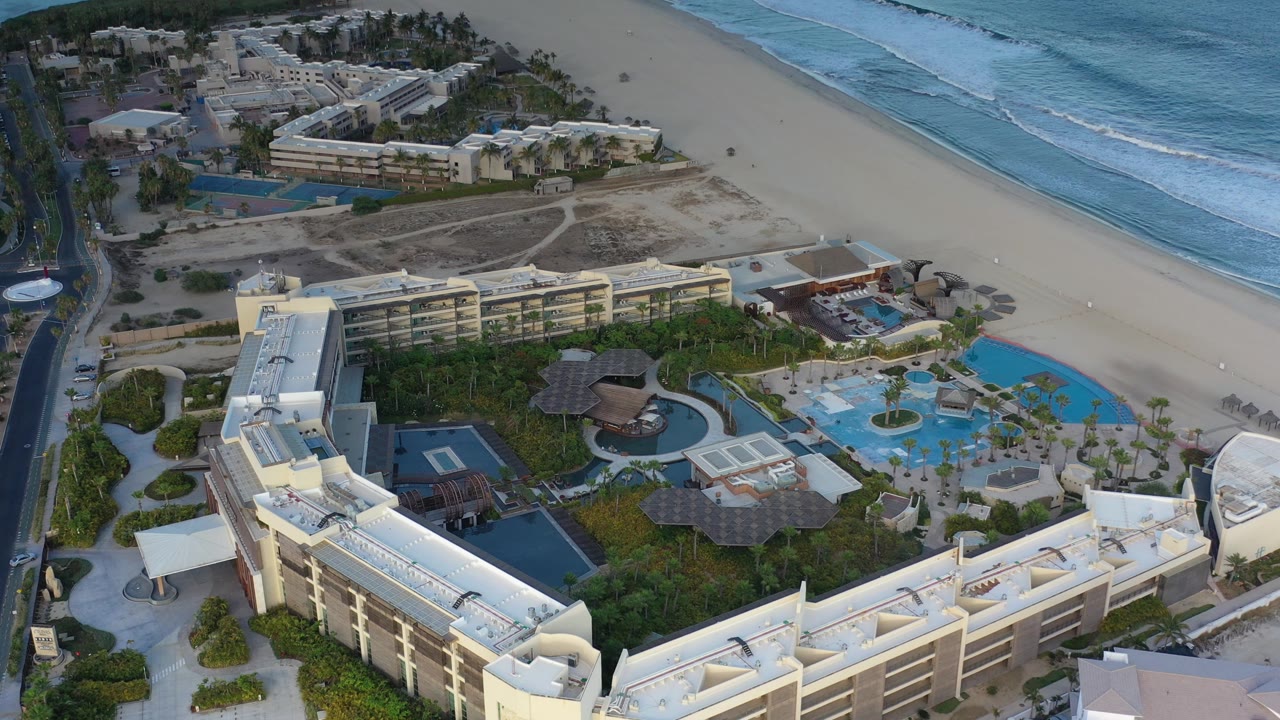 Aerial resort view with pools, palm grounds, beach, and ocean waves.