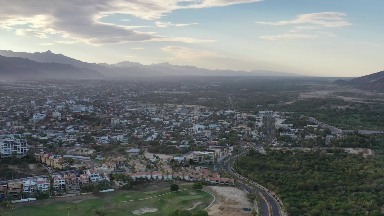 High city view with dense greenery, rooftops, mountains, and evening sky.