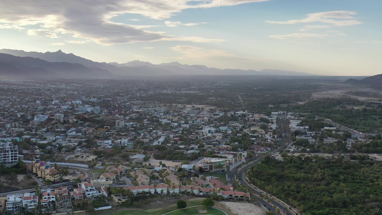 Aerial view of a city below mountains and a cloudy sky.
