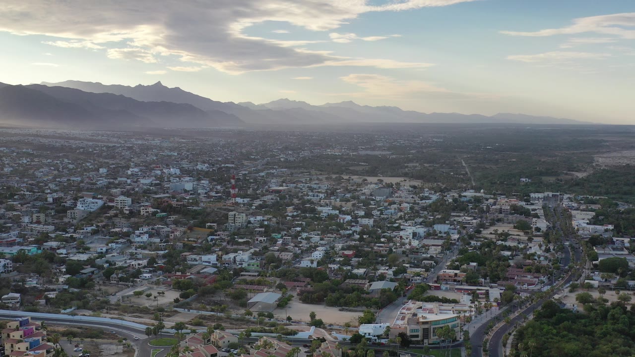 Wide aerial view over a town with mountains and cloudy blue sky.