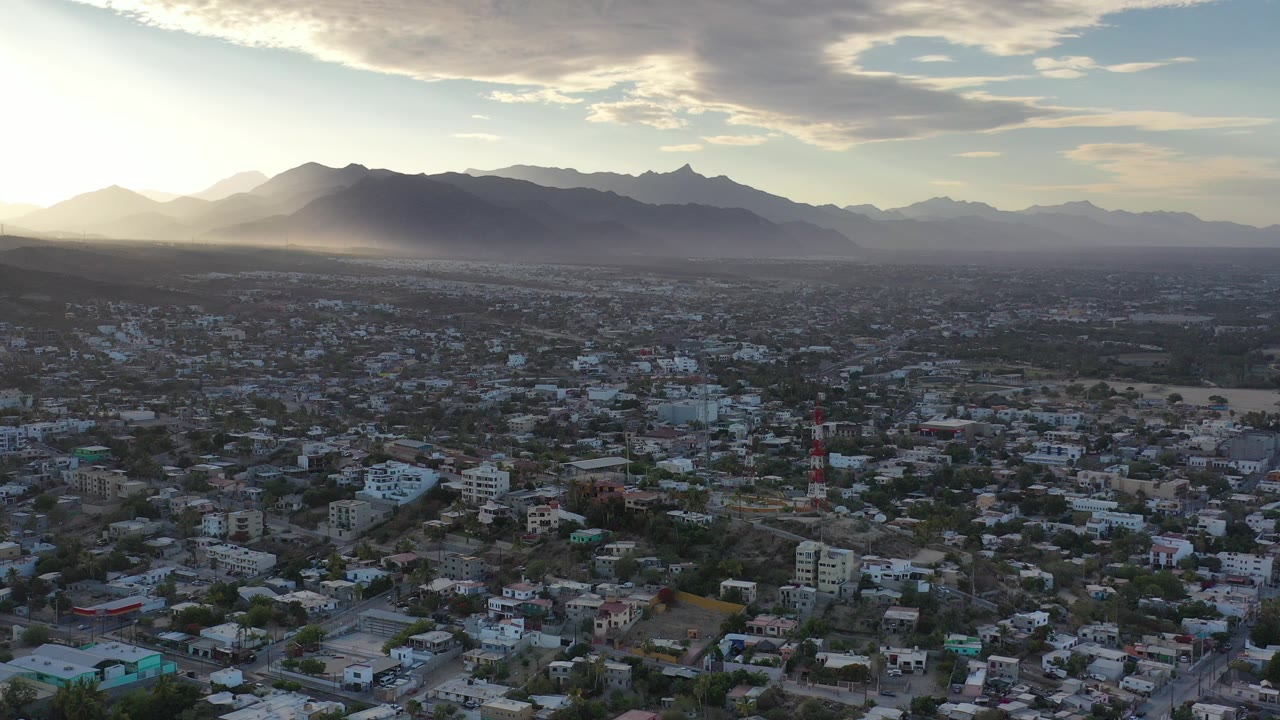 Aerial view of a large town below mountains at low sun.