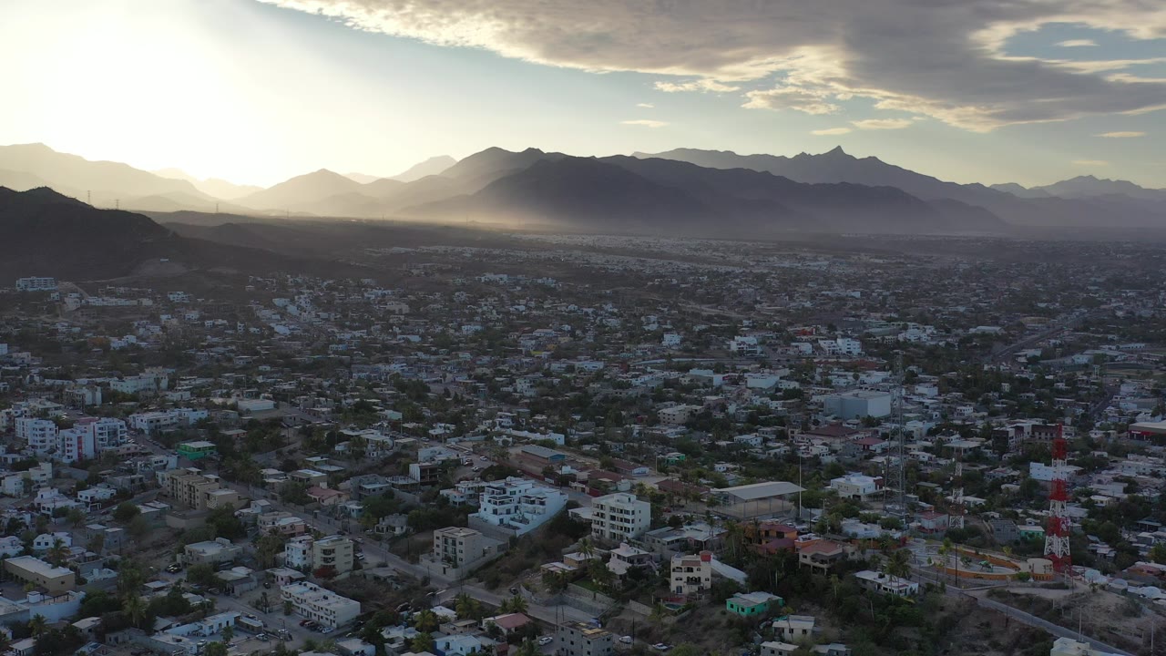 Aerial city view with mountains and bright sun near the horizon.