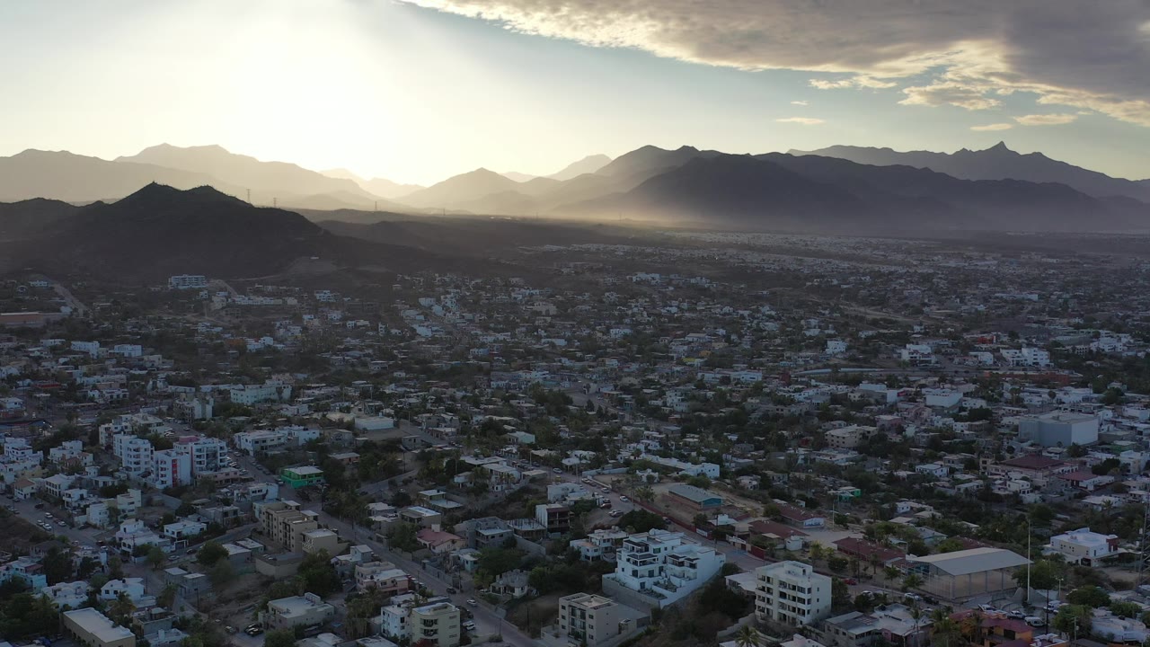 Sunlight breaks through cloud over sprawling city and mountain horizon.