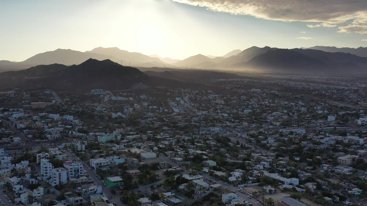 Aerial view of a city below mountains at sunrise.