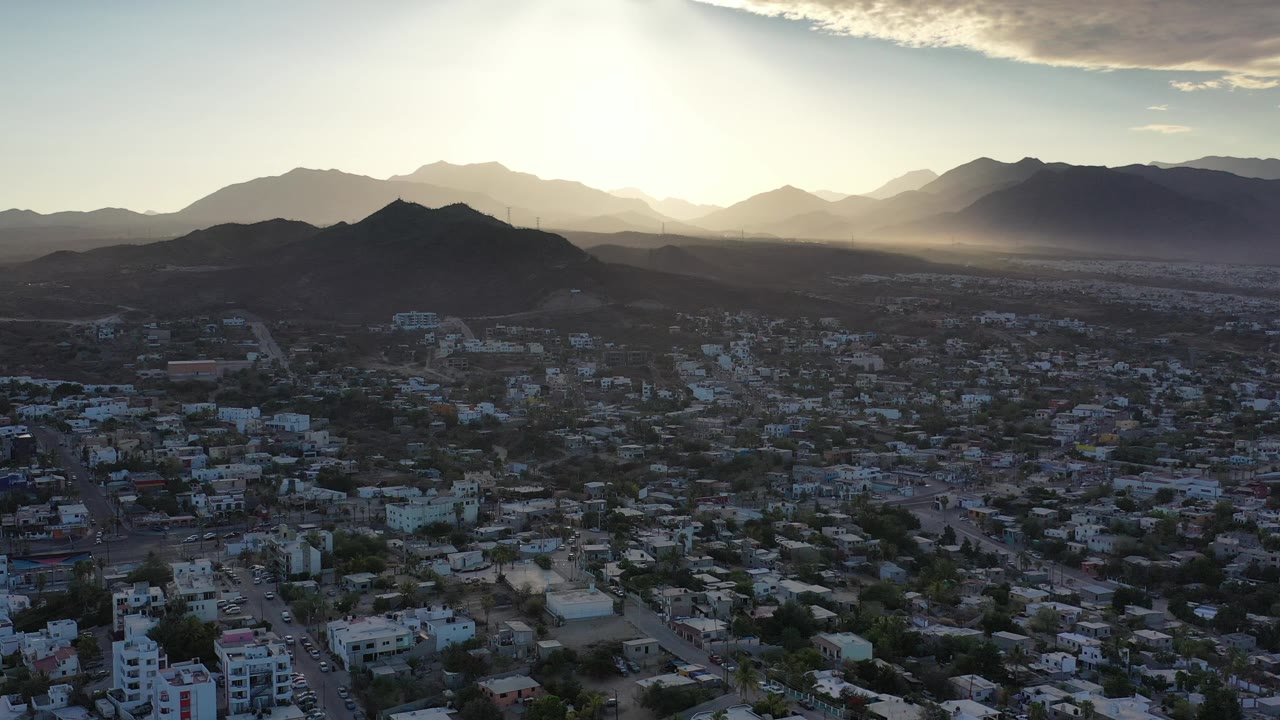 Wide aerial of buildings, roads, hills, and distant mountains.