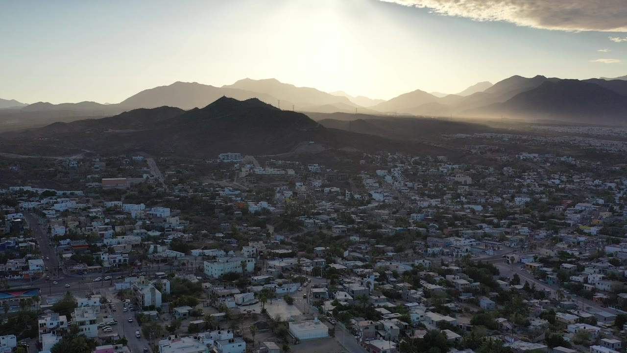 Aerial view of a city below mountains with bright sun haze.
