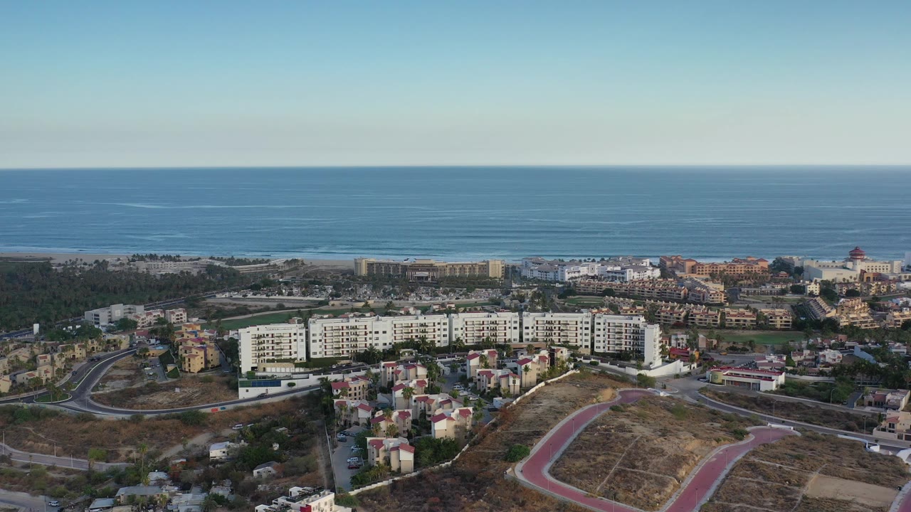 Coastal town seen from above with ocean, roads, apartments, and dry lots.