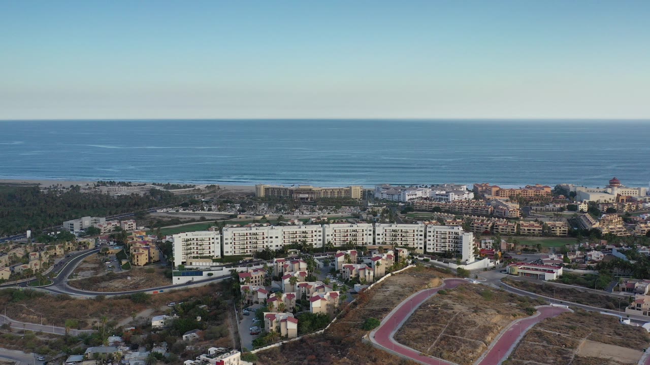 Aerial view of coastal resort buildings, hillside roads, and blue ocean horizon.