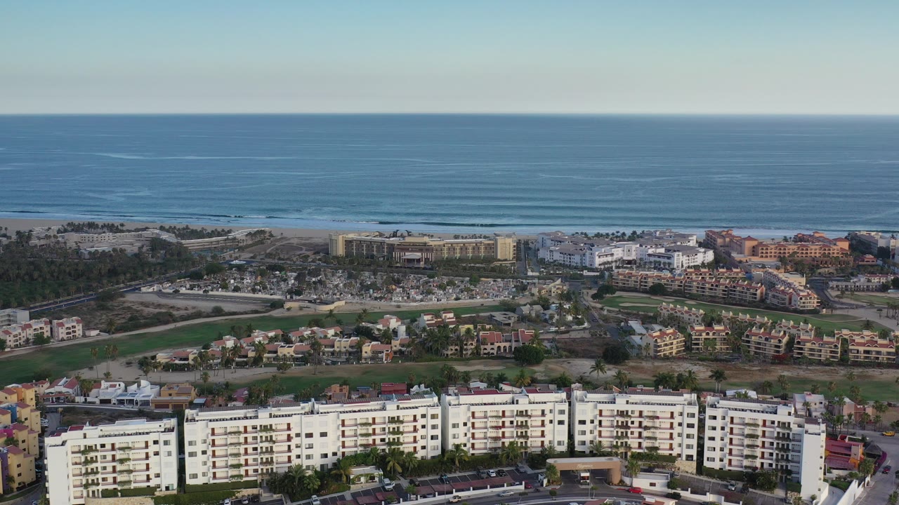 Aerial view of ocean, beach, coastal roads, villas, and mid-rise buildings.