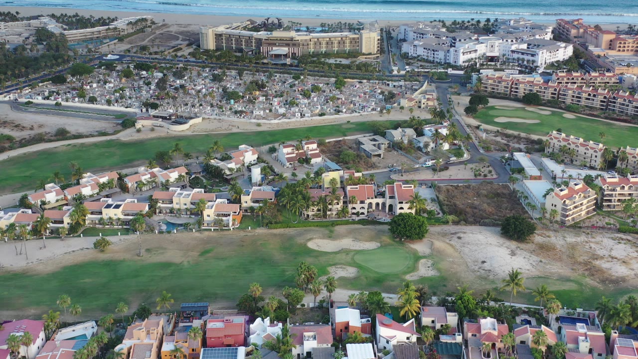 Aerial view of golf greens, houses, roads, cemetery, and coastal water.