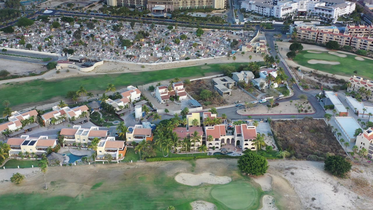 Aerial view of homes, roads, golf-course grass, and dense housing beyond.