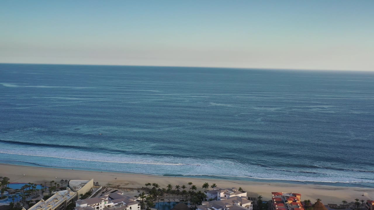 Clear sky over open ocean with waves breaking near a beach.