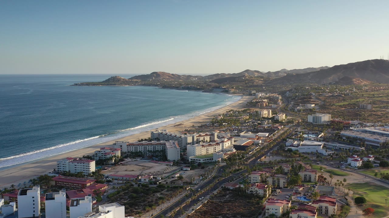 Aerial view of ocean, beach, resort buildings, roads, and hills.