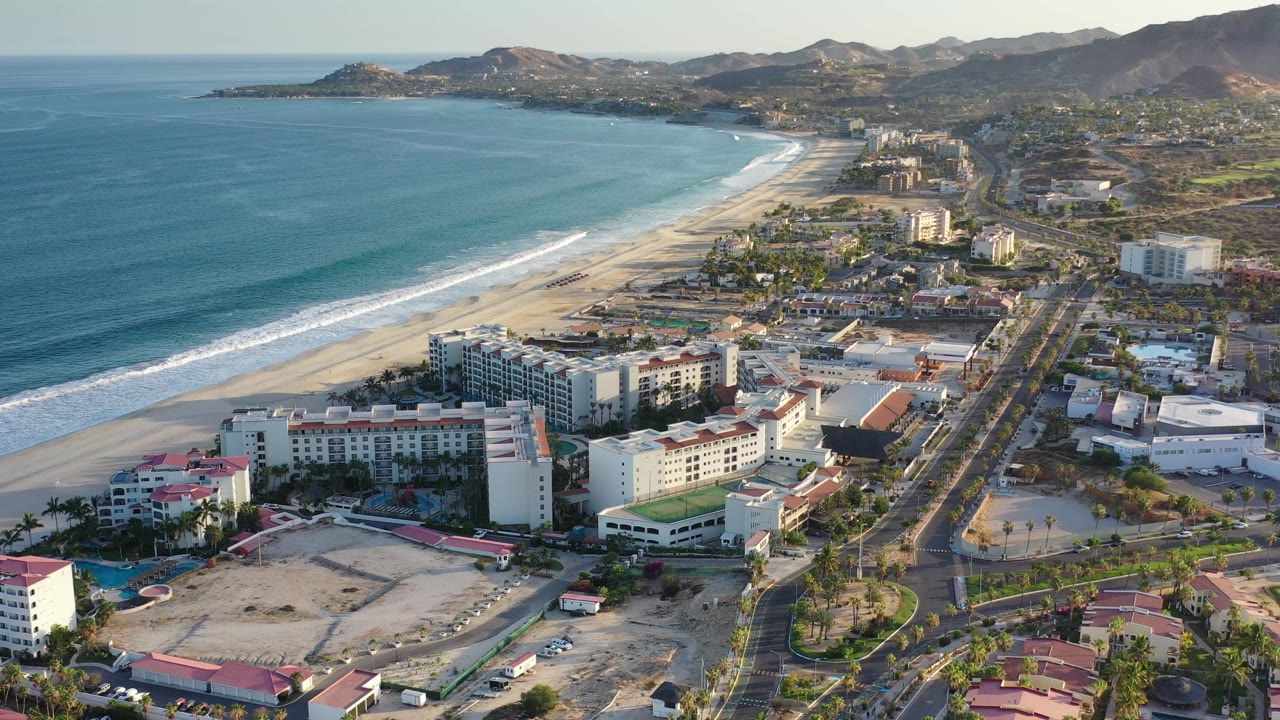 High aerial view of beach, ocean, resort buildings, and mountains.