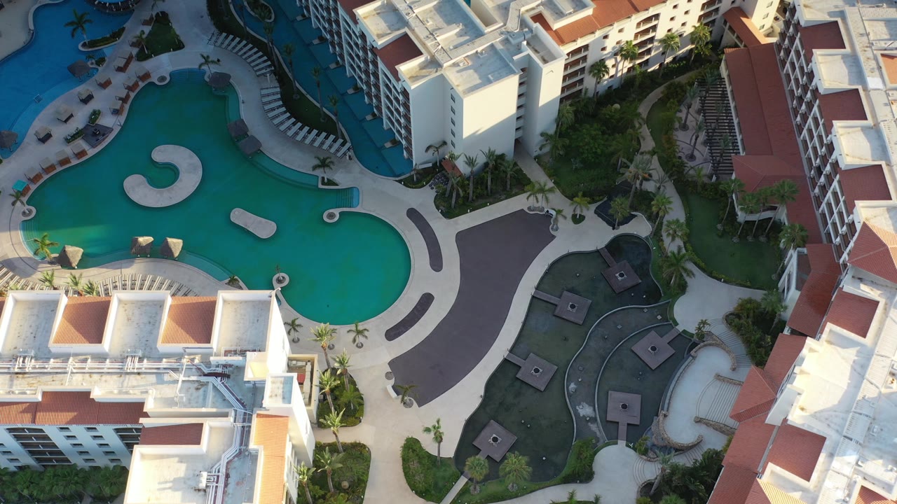 Drone view of pools beside multi-story buildings and landscaping.