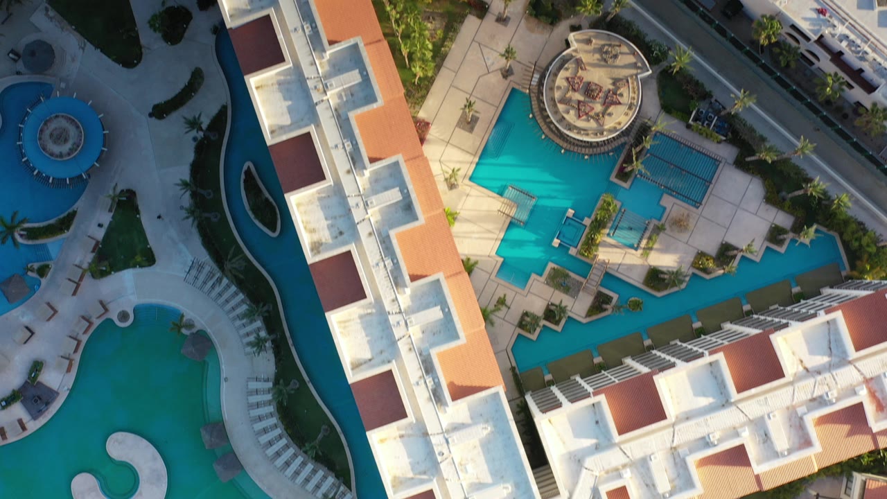 Overhead resort buildings and turquoise pools beside sand and palms.