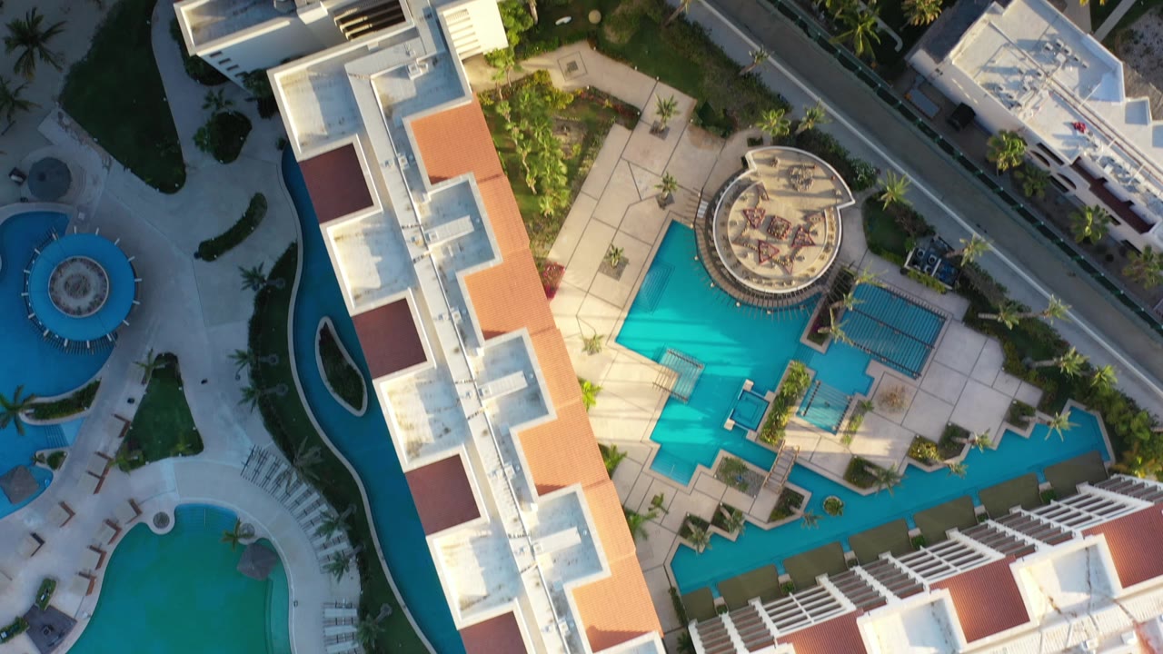 Aerial resort rooflines, pool deck, road, and palms.