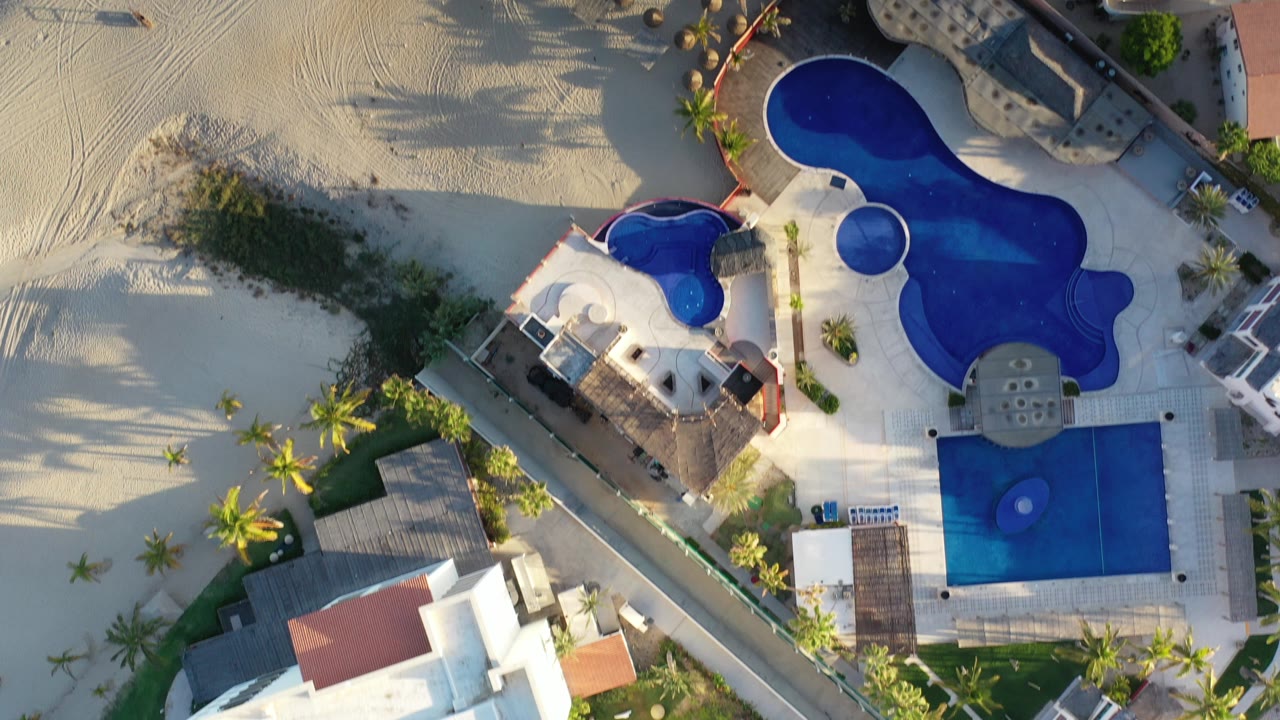 Overhead view of blue swimming pools beside pale sand and palm trees.