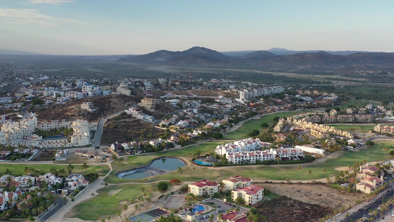 Aerial neighborhood view with fairways, ponds, dry hills, and distant mountains.