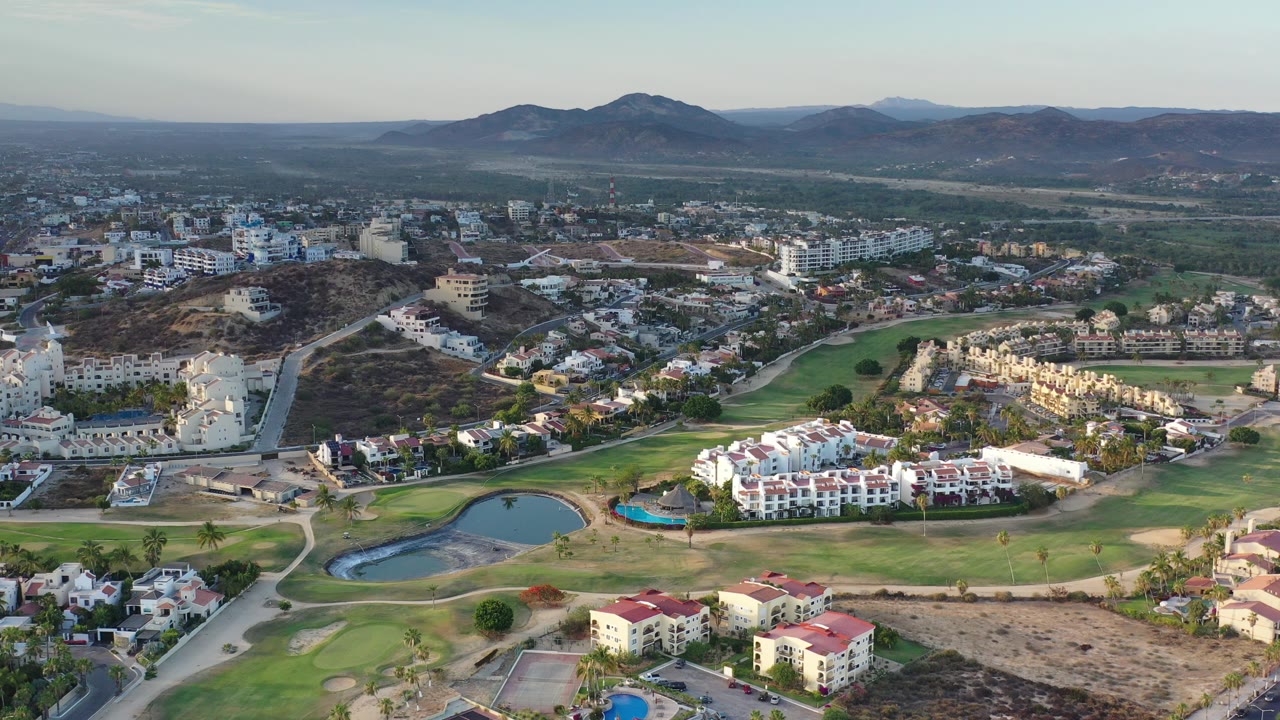 Aerial view of golf course, buildings, roads, and mountains.