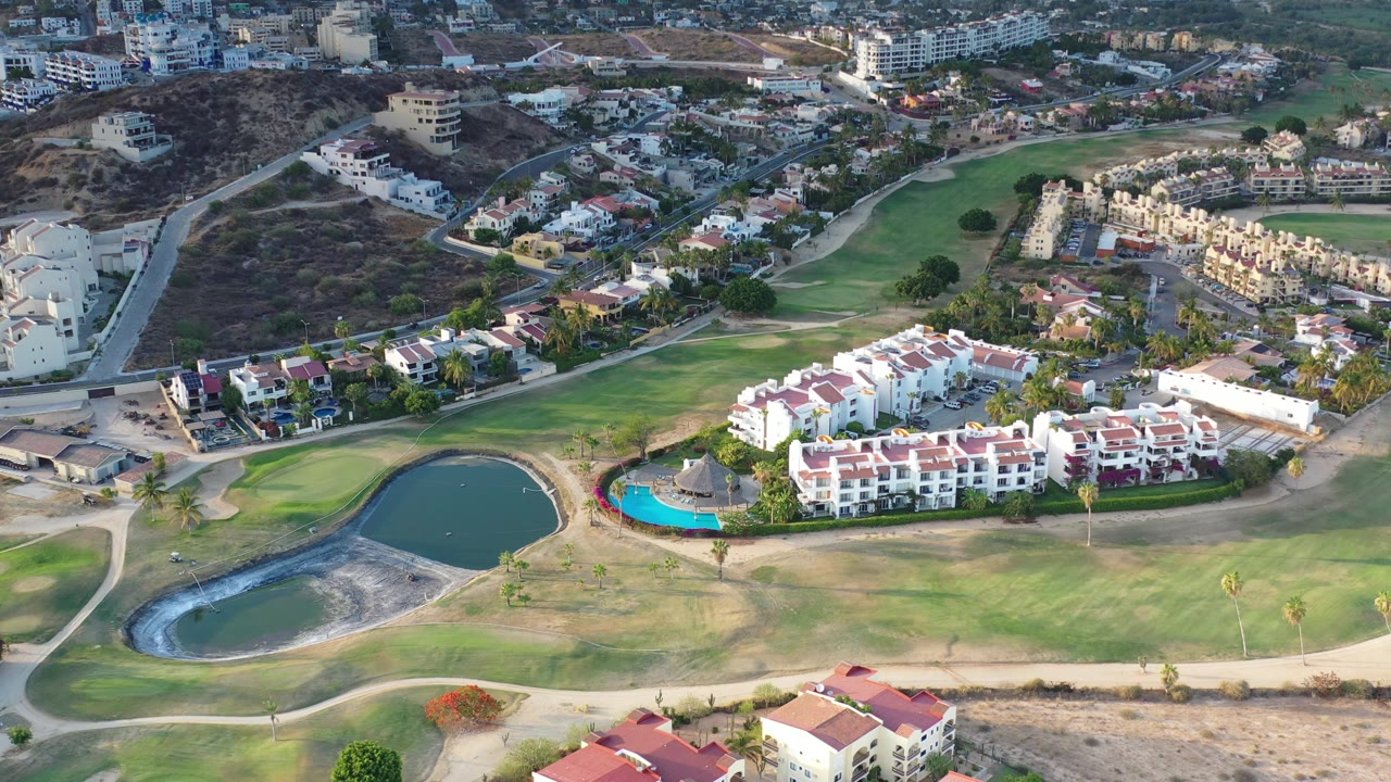 Drone view of golf greens bordered by homes and roads.