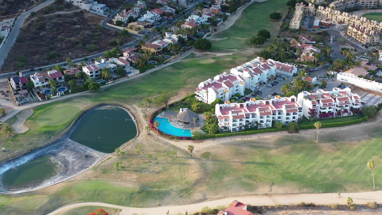 High aerial of apartments, pool area, ponds, fairways, roads, and homes.