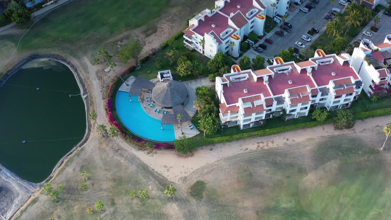 Overhead view of red-roofed buildings beside a blue pool and dark pond.