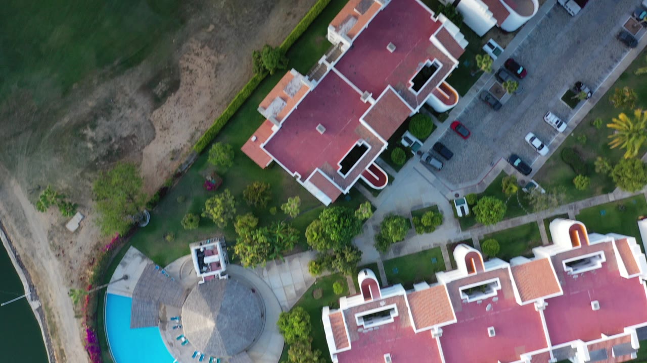 Overhead view of red-roofed buildings beside a green grass field and parked cars.