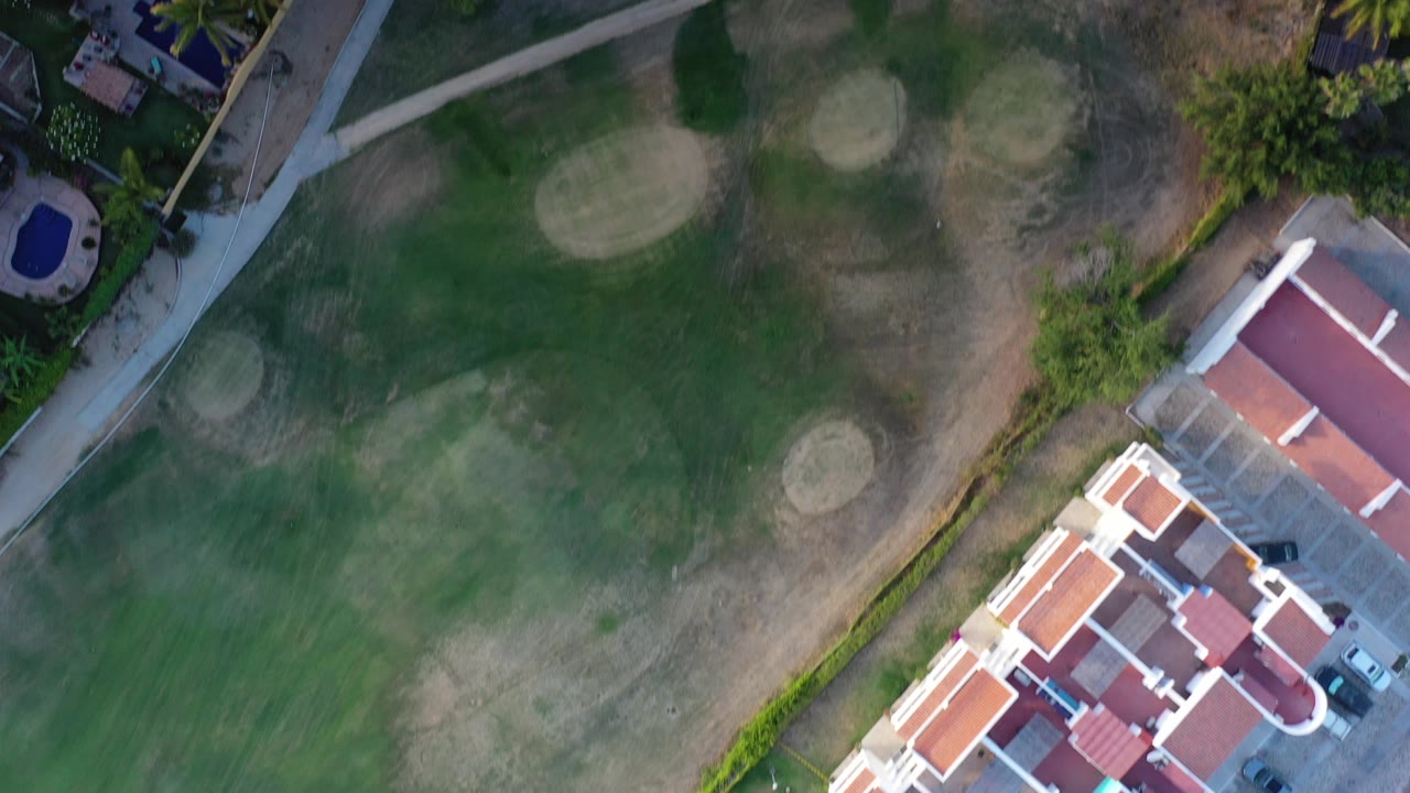 Overhead view of golf course grass, red-roofed homes, pools, roads, and trees.
