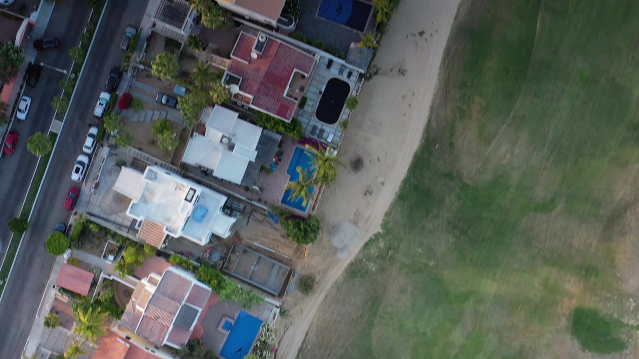 Top-down aerial view of houses beside a road and green field.