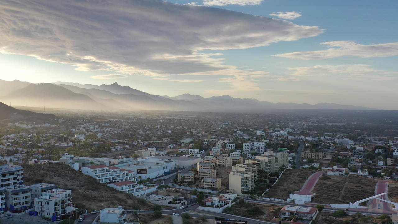 Aerial town view below hazy mountains and broad clouds.
