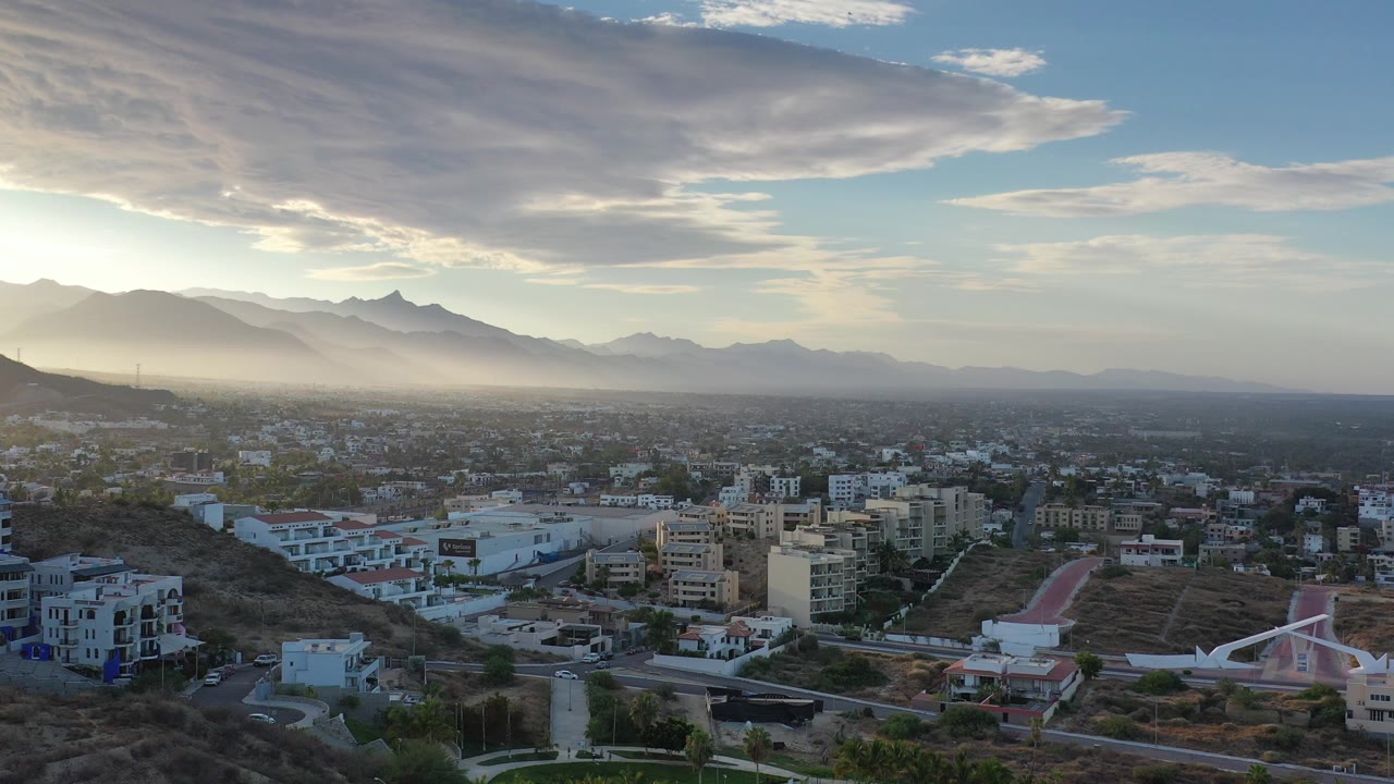 Aerial city view below hazy mountains and sunrise clouds